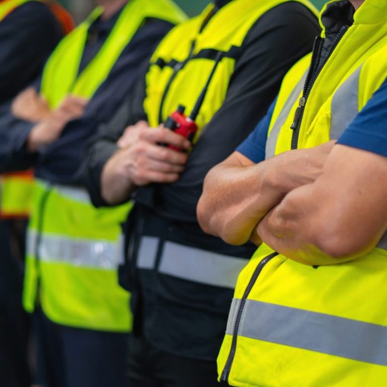 group of men in yellow safety vests stand together. They are all wearing the same type of vest and are all wearing the same color